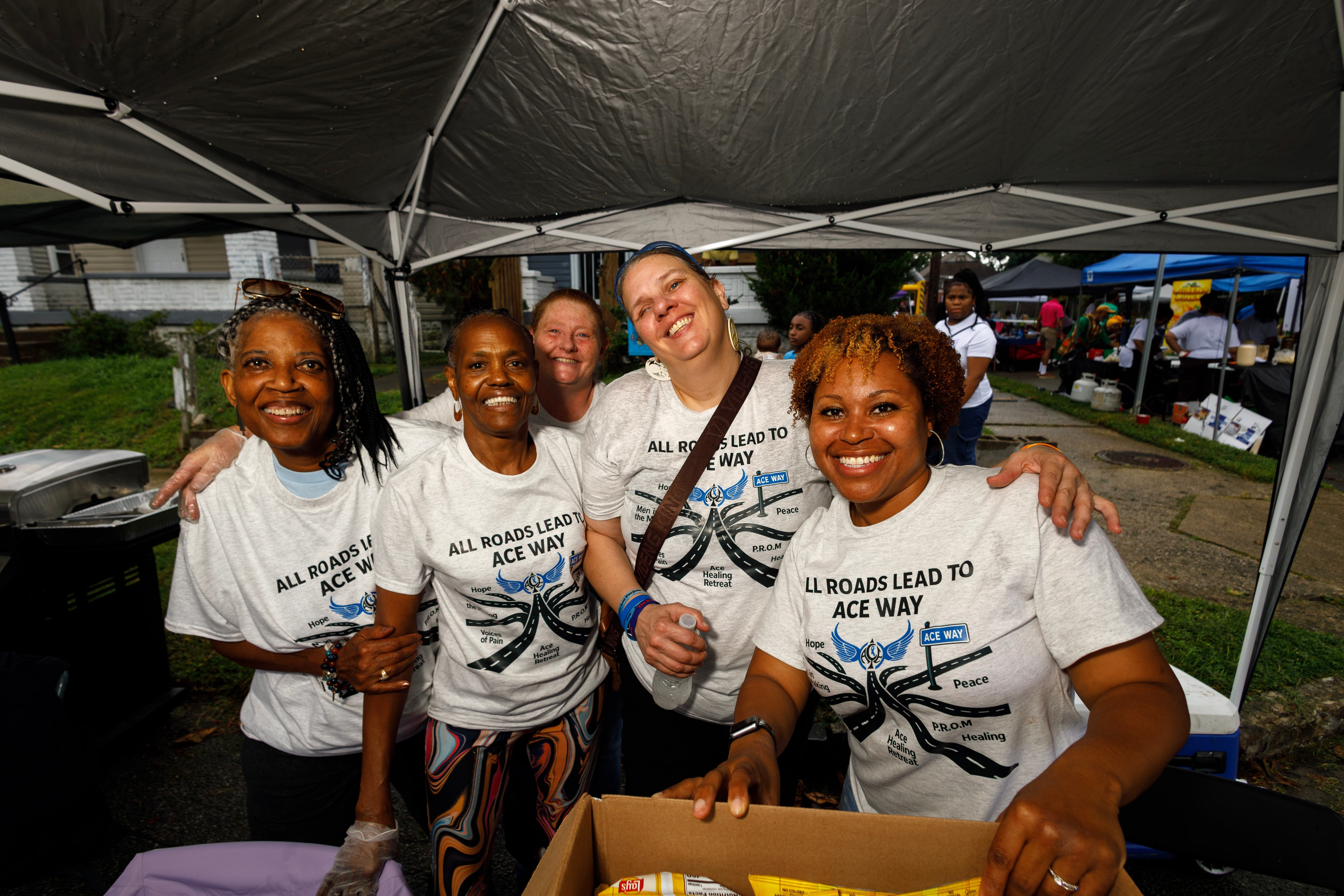 Five ACE Project volunteers in All Roads Lead to ACE Way shirts smiling together
