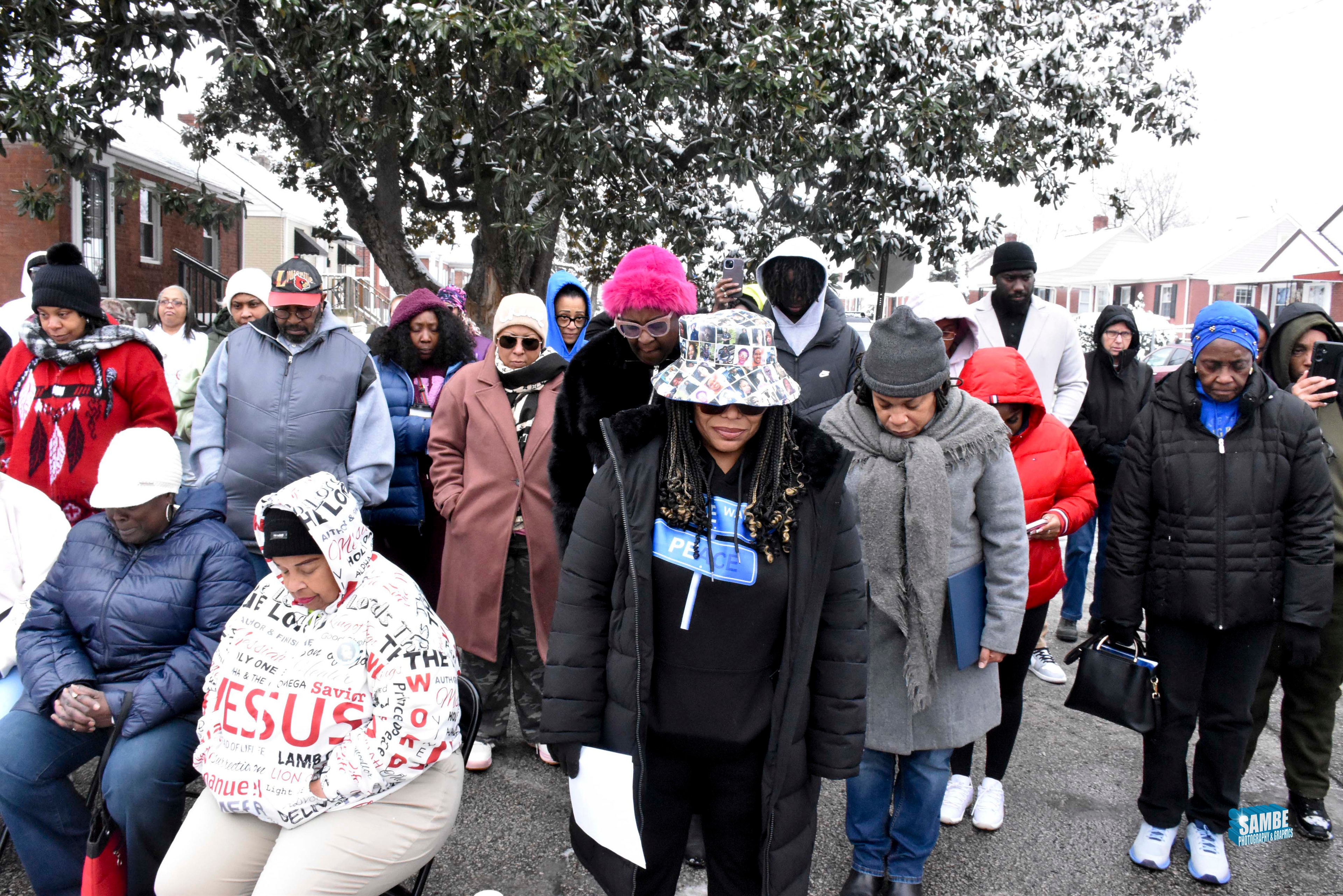 Community members gathered in prayer outdoors in winter clothing at ACE Project vigil