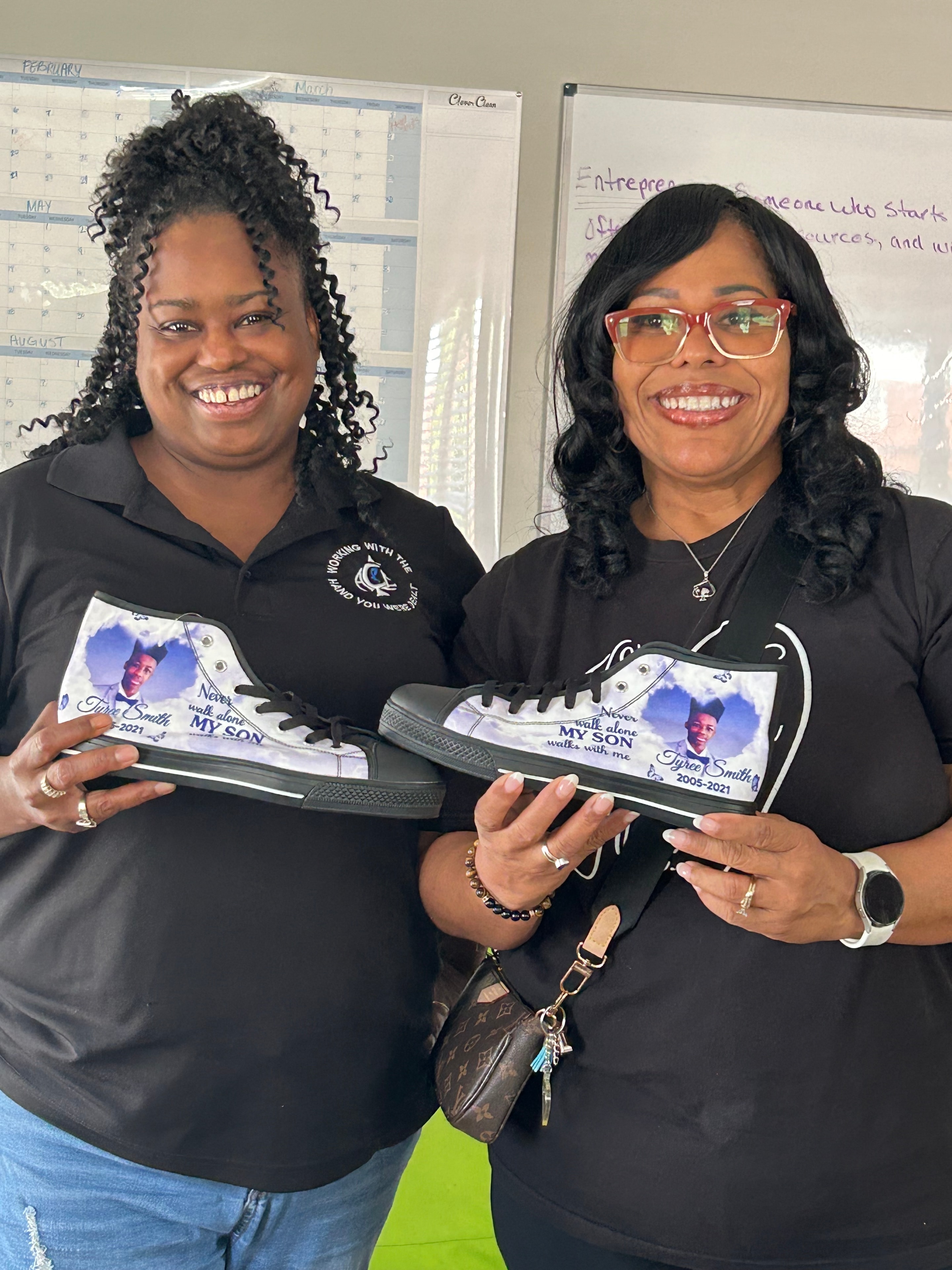 Two women holding custom memorial sneakers honoring Tyree Smith at ACE Project event