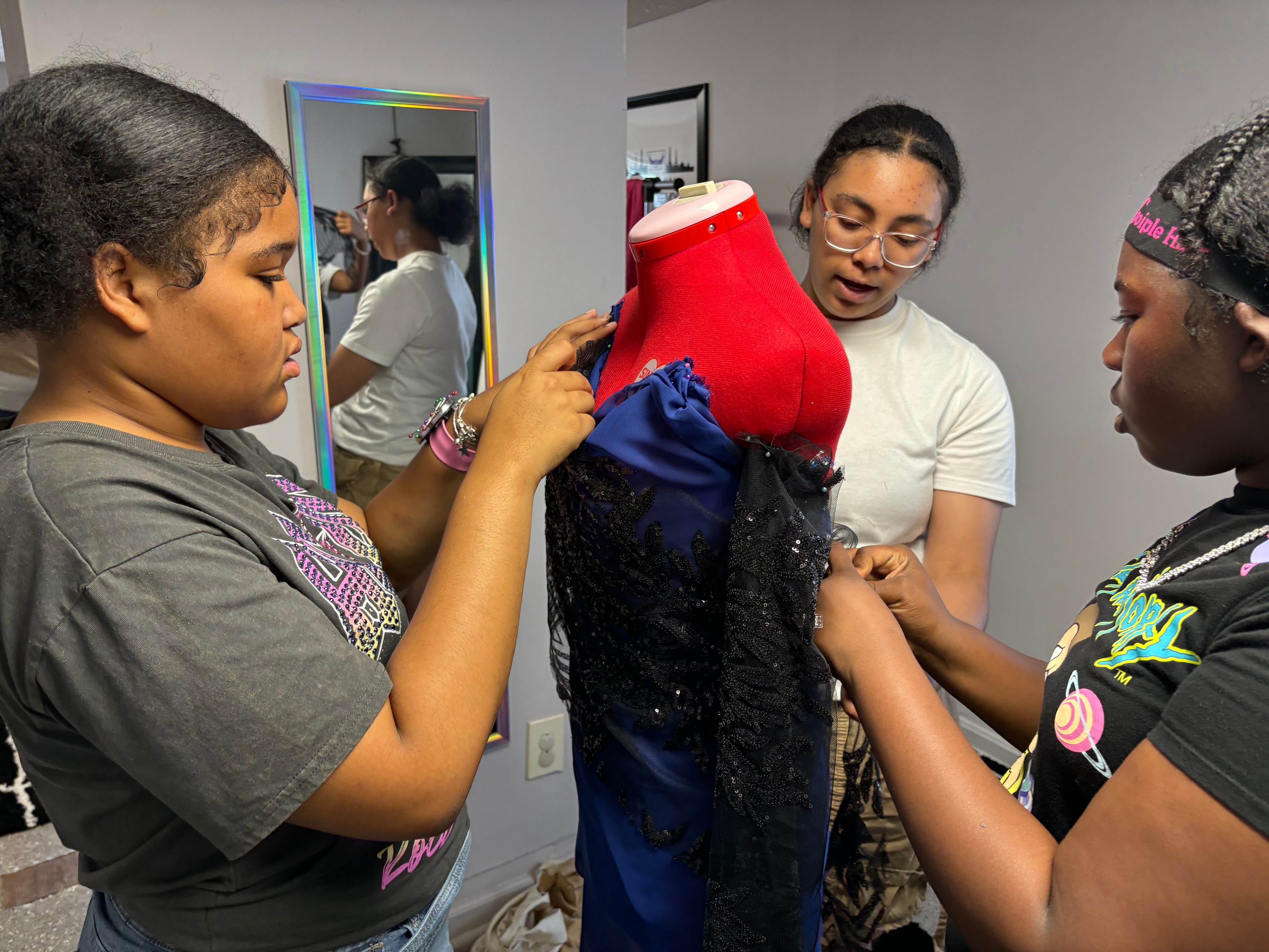 Three young women working on a dress design on a mannequin at ACE PROM sewing program