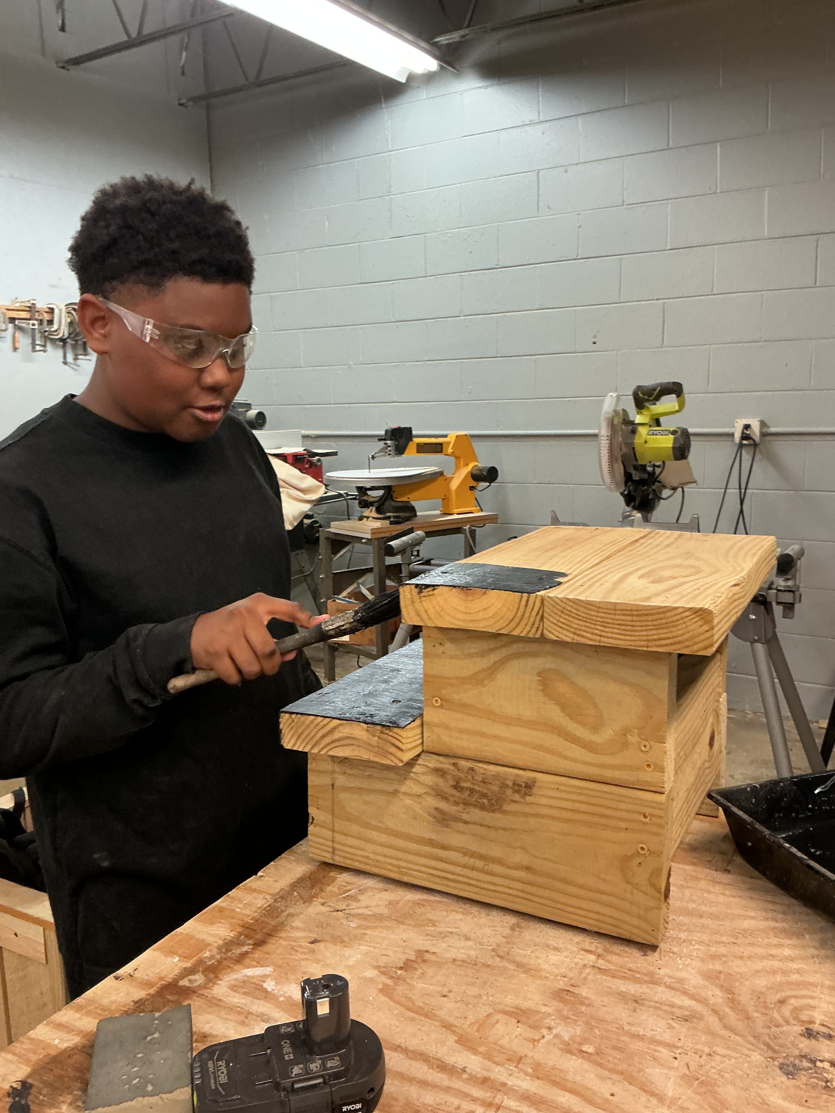 Youth participant inspecting a wooden box he built in the ACE Project woodshop