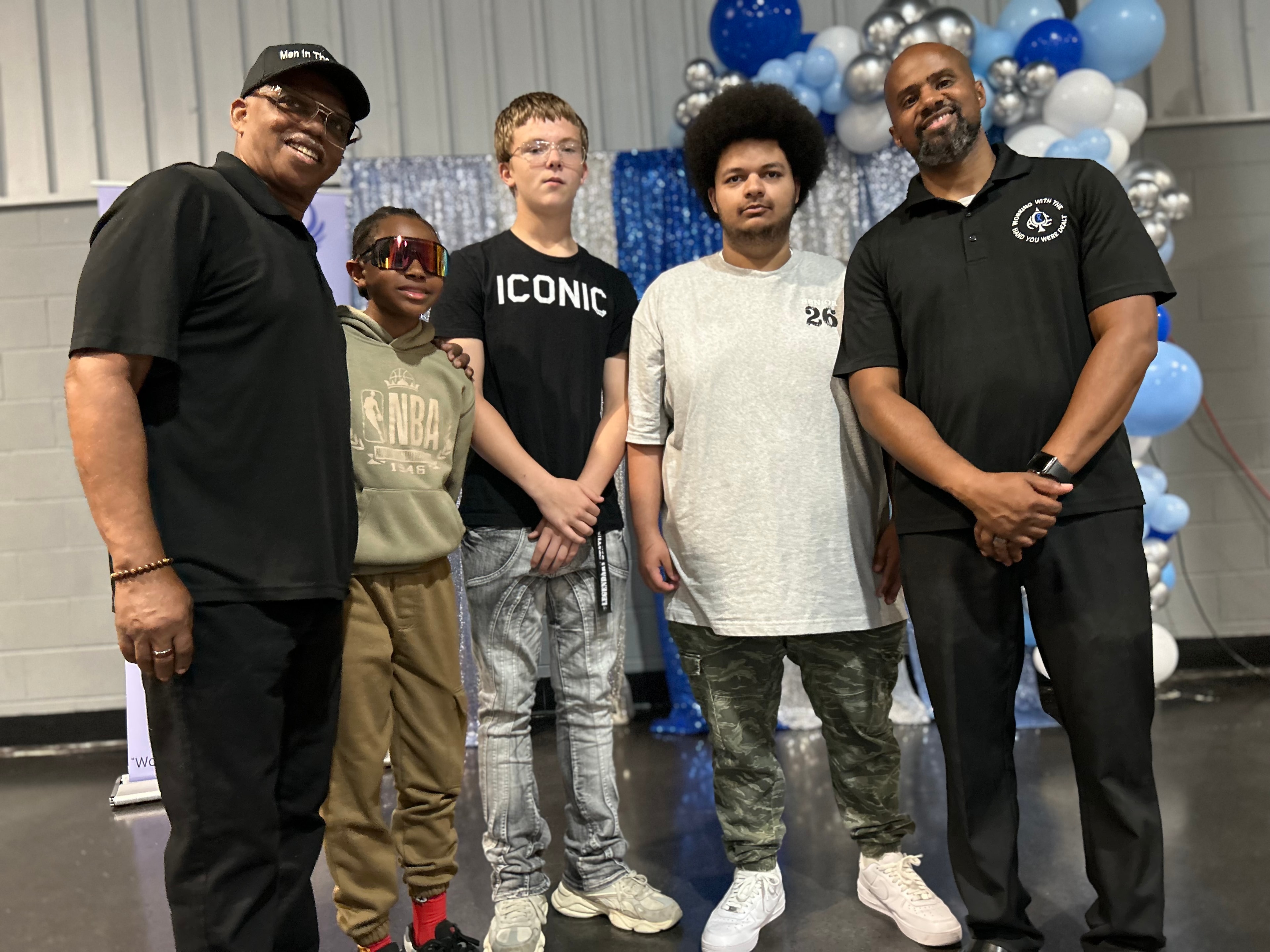 Walter Smith and youth participants posing at Men in the Making graduation ceremony with blue and silver balloons