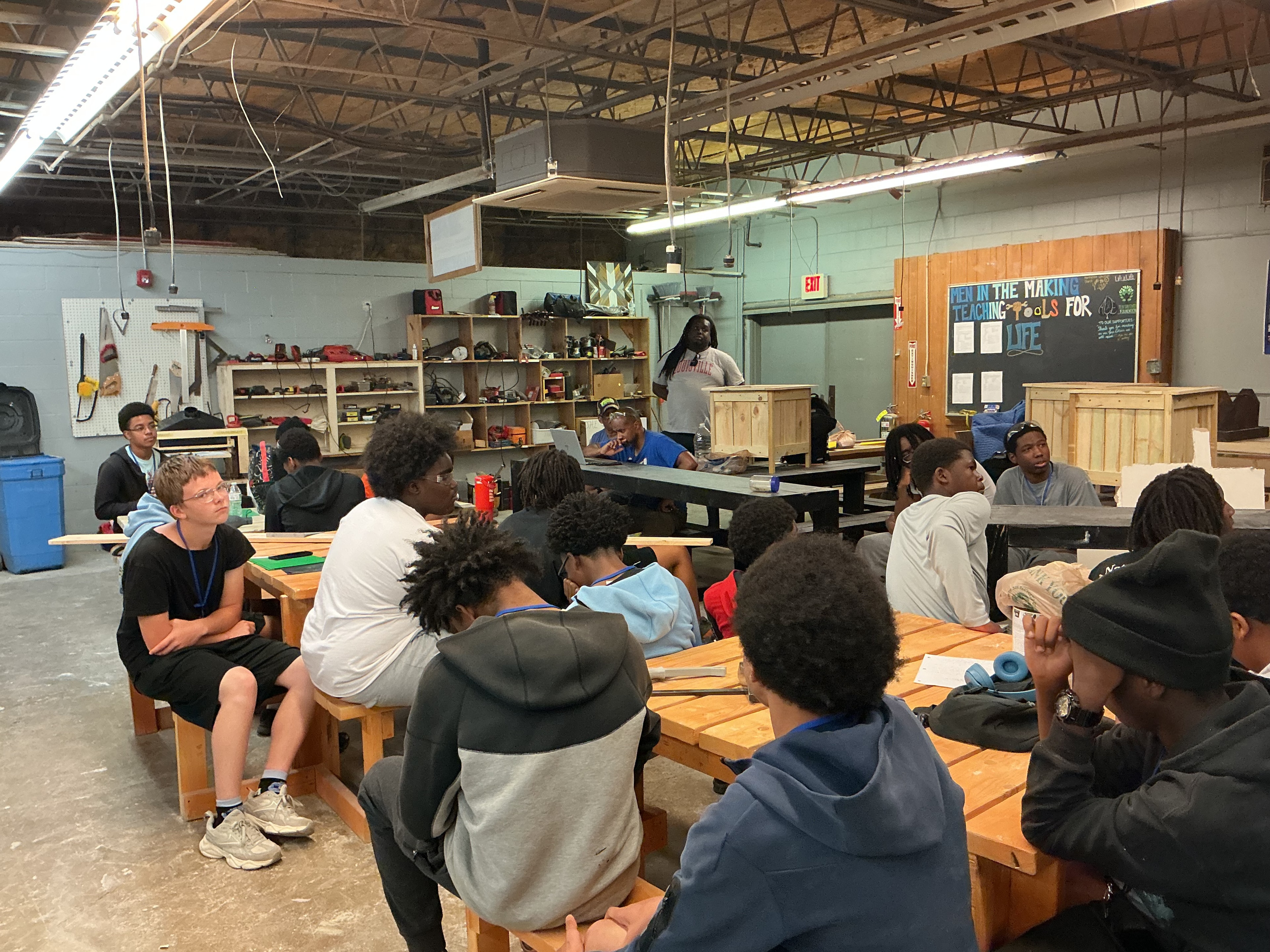 Large group of youth seated in the Men in the Making woodshop classroom for a lesson